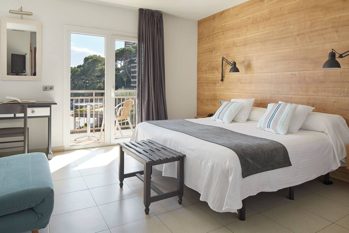 A bedroom with a bed, bedside table, chair, and a view of the outdoors.