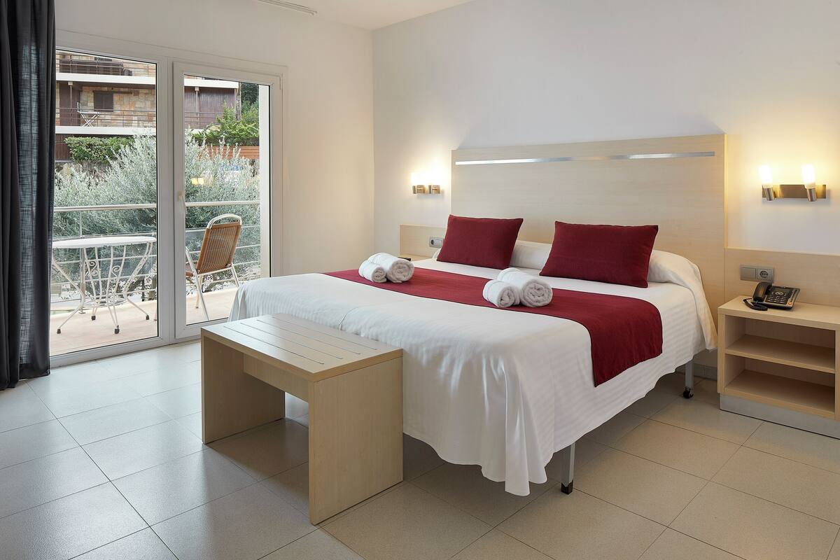 A hotel room with a bed, a bedside table, a desk, and a view of the outside balcony.