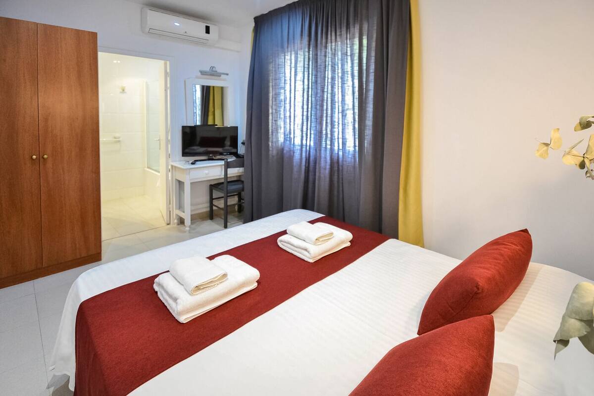 A hotel room with a bed, two pillows, a desk with a computer, a TV, and a wardrobe.