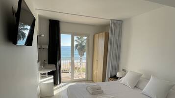 Una habitación de hotel con una cama grande, un televisor montado en la pared, un baño con lavamanos y vistas a la playa.