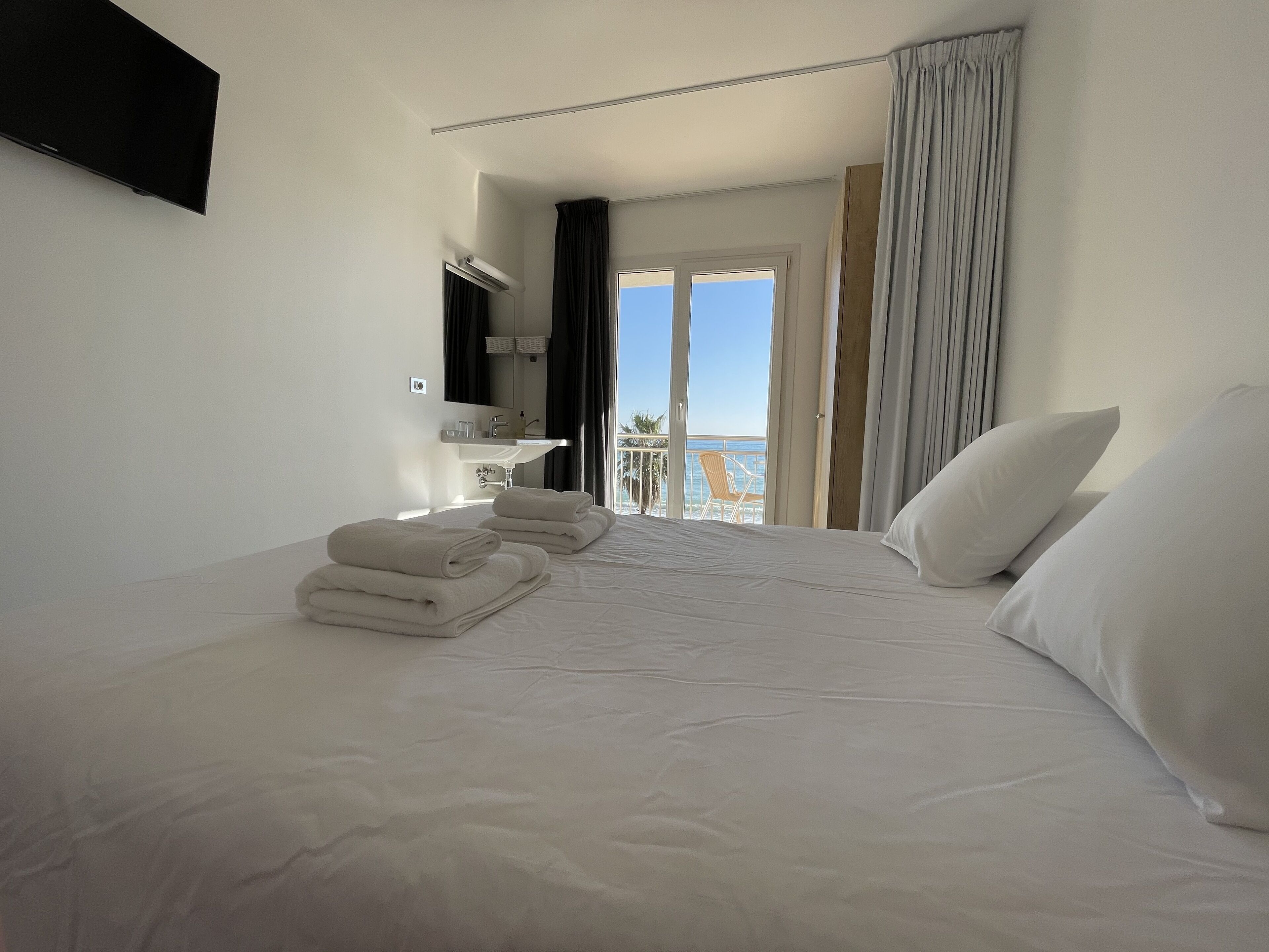 A hotel room with a bed, towels, a bathroom, and a balcony with a view.