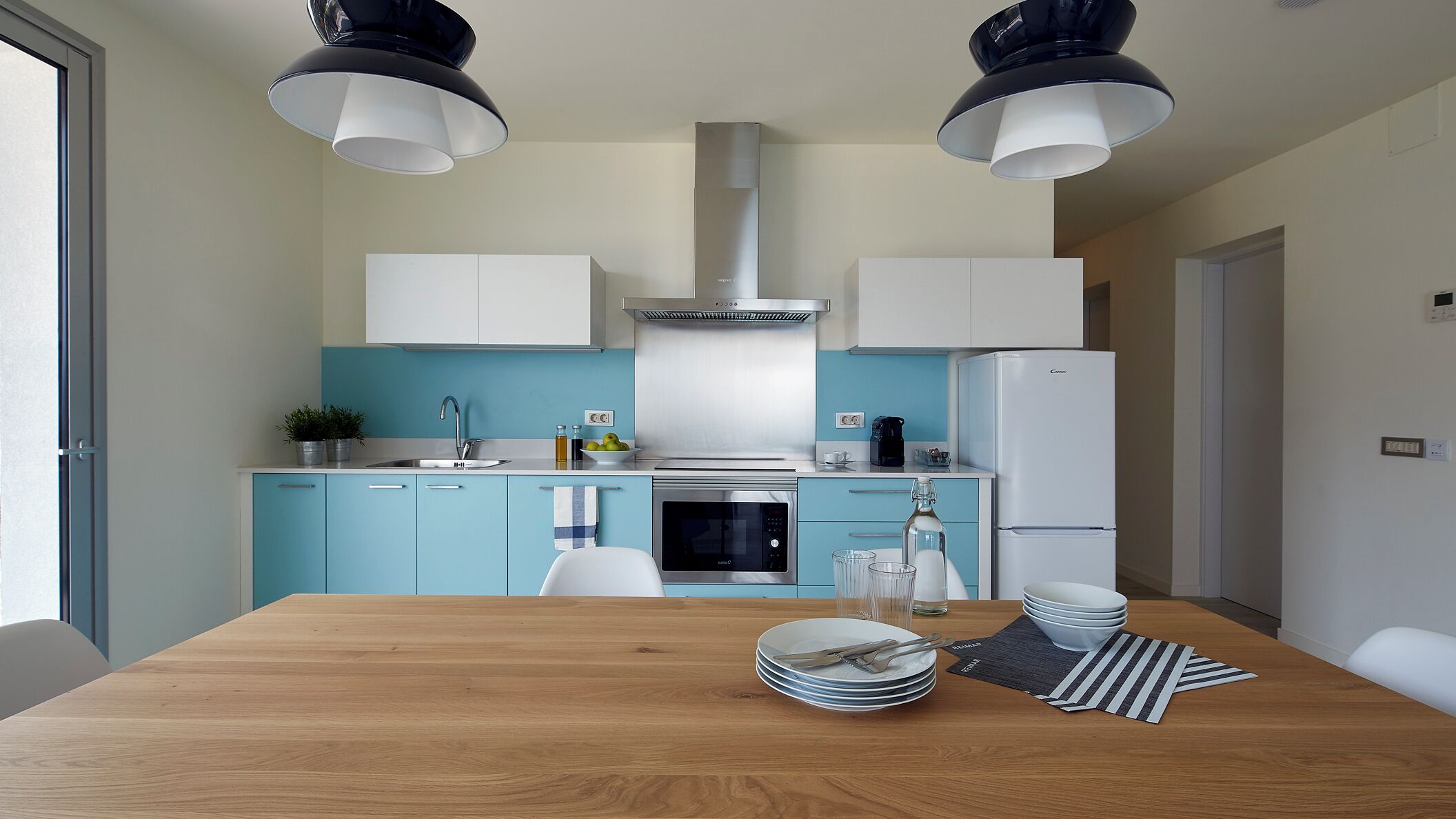 A modern kitchen with a wooden dining table, white cabinets, and stainless steel appliances.