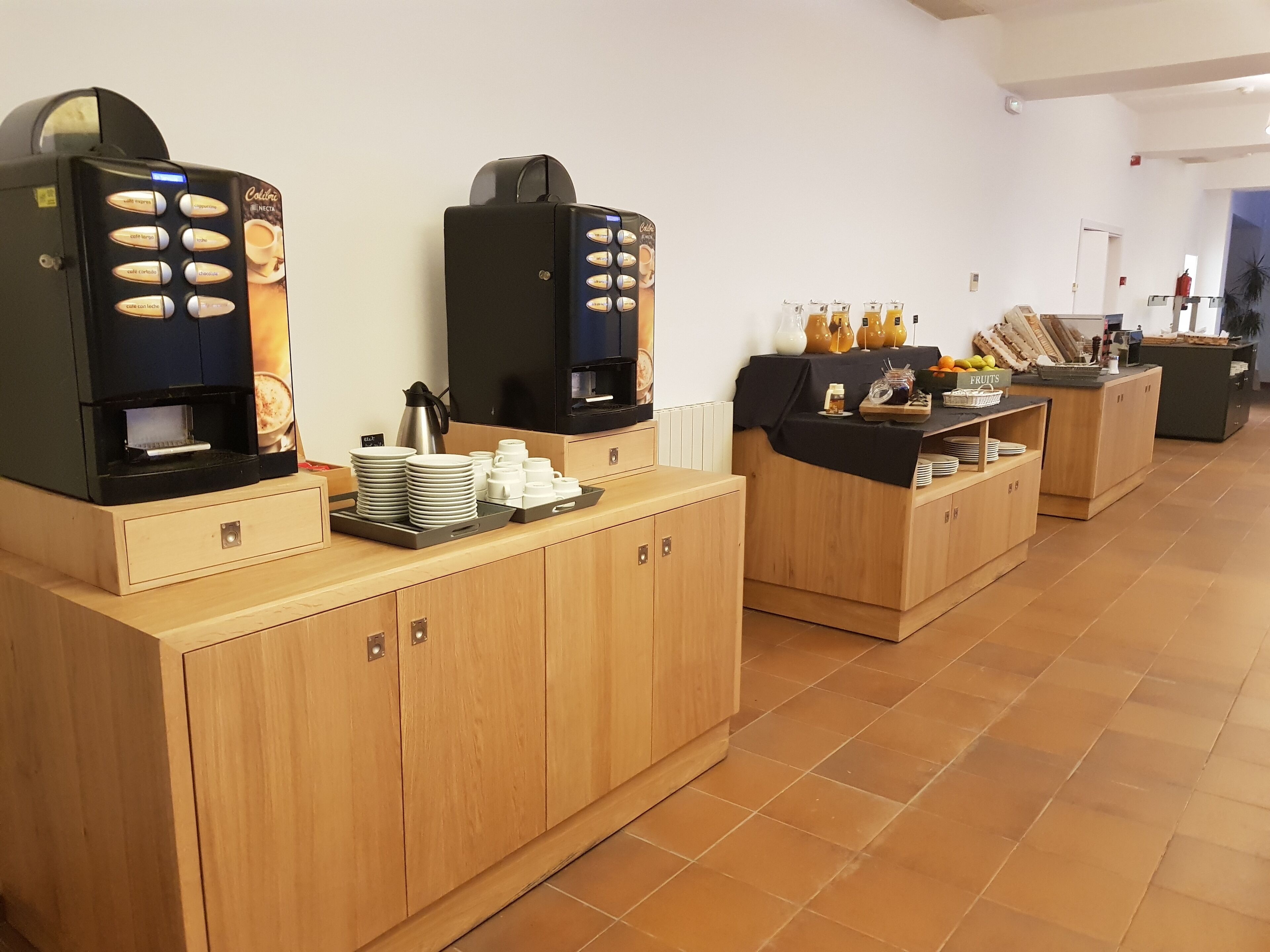 Habitación de hotel con kitchenette que incluye dos máquinas de café, una cafetera y una exposición de frutas.