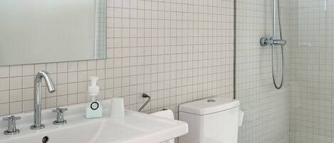 Un baño moderno con un lavamanos blanco, un inodoro y una ducha.