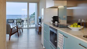 A modern kitchen with a view to the sea, featuring a large island, stainless steel appliances, and light blue cabinets.