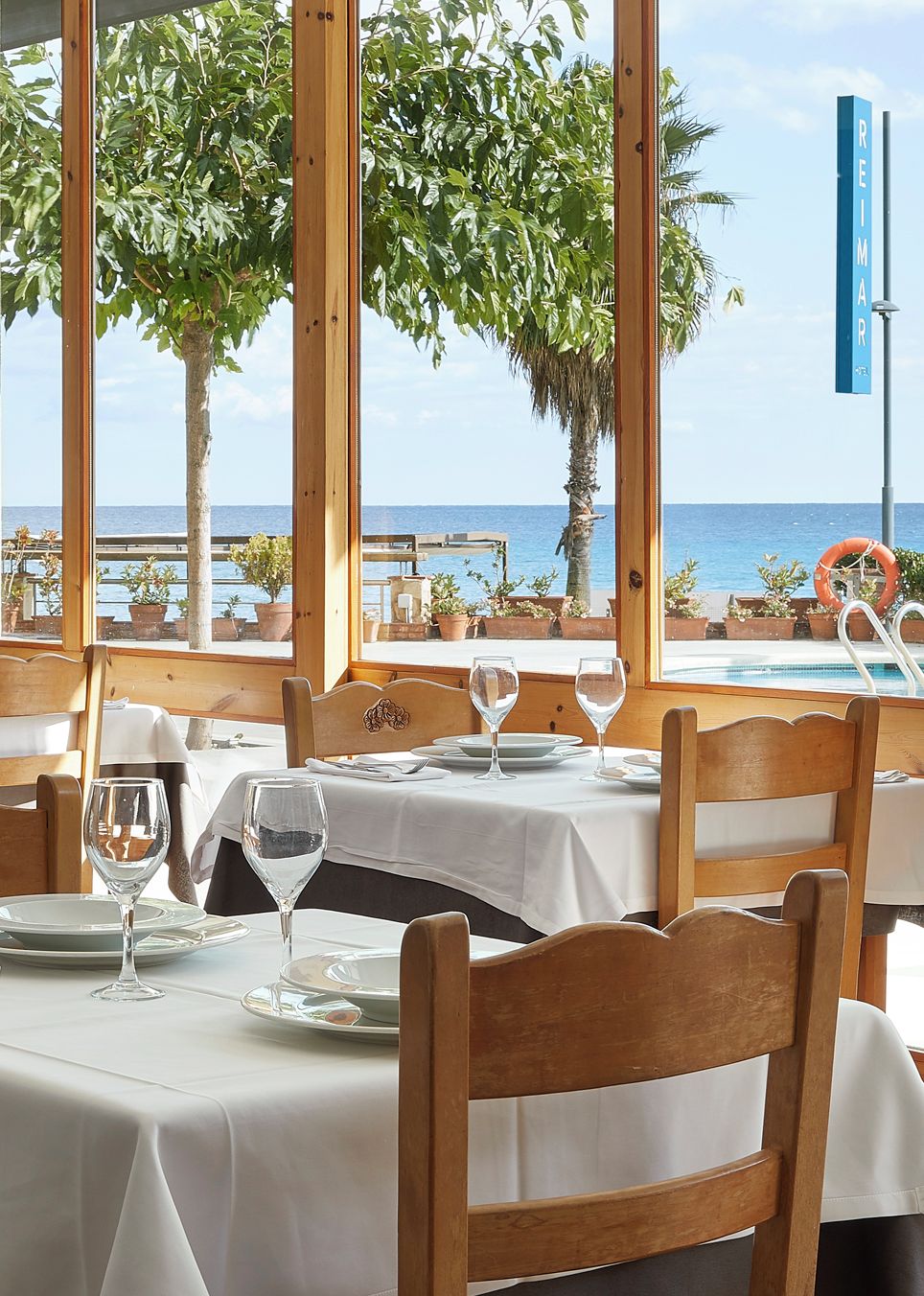 Un comedor con mesas preparadas para dos, con vistas a una playa y una vista despejada del mar.