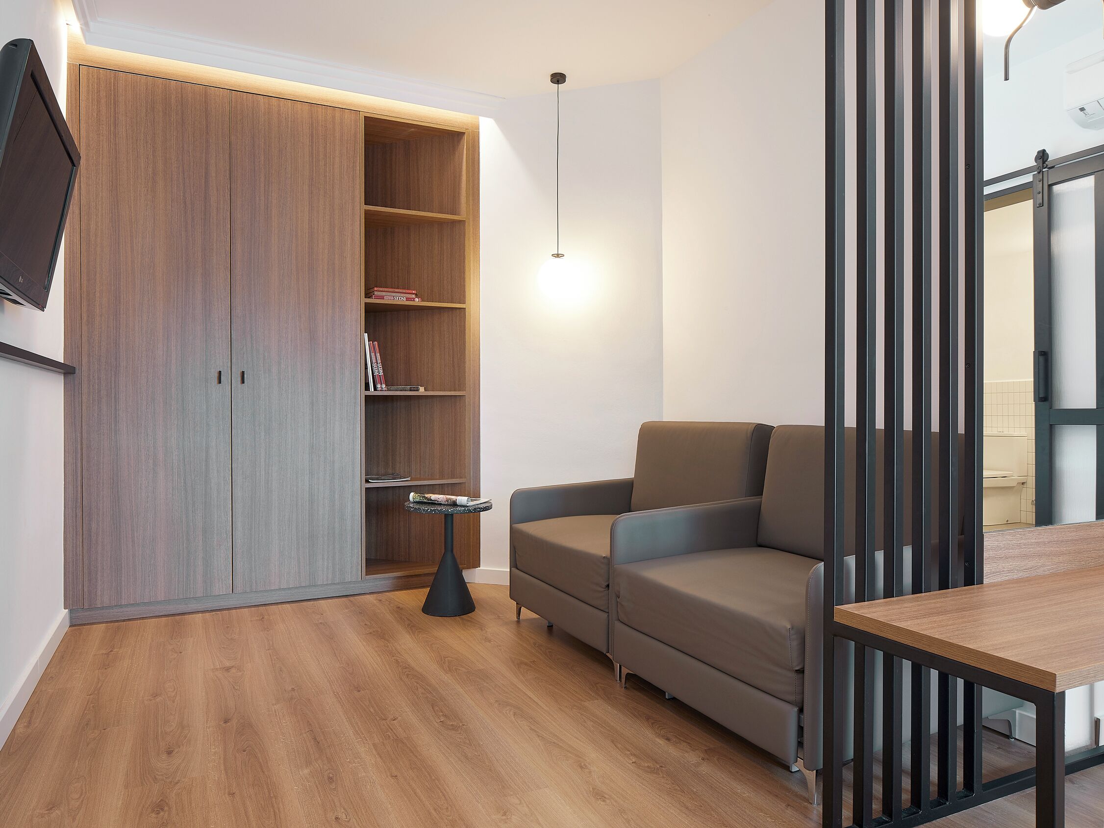 A modern living room with a wooden floor, a grey sofa, a small round table, and a bookshelf.