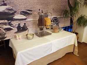 A buffet table with a white tablecloth, a coffee grinder, a bowl with a spoon, and containers of food items.