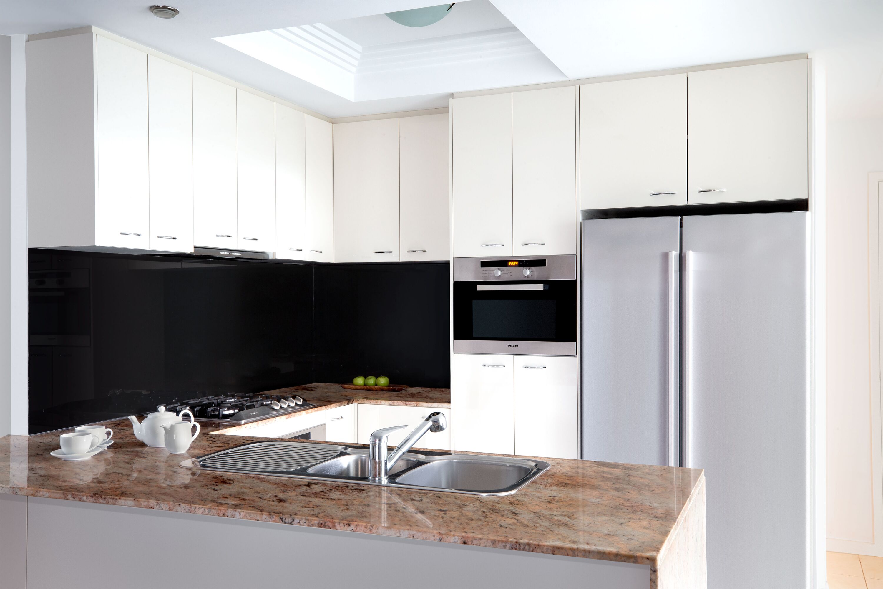 A modern kitchen with white cabinets, a stainless steel refrigerator, a built-in oven, and a gas stove.