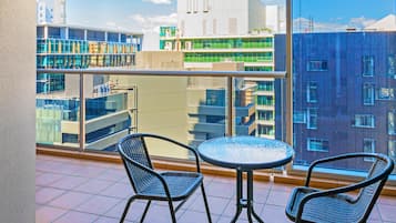 A balcony with two wicker chairs and a round table, overlooking a modern building with multiple floors and large windows.