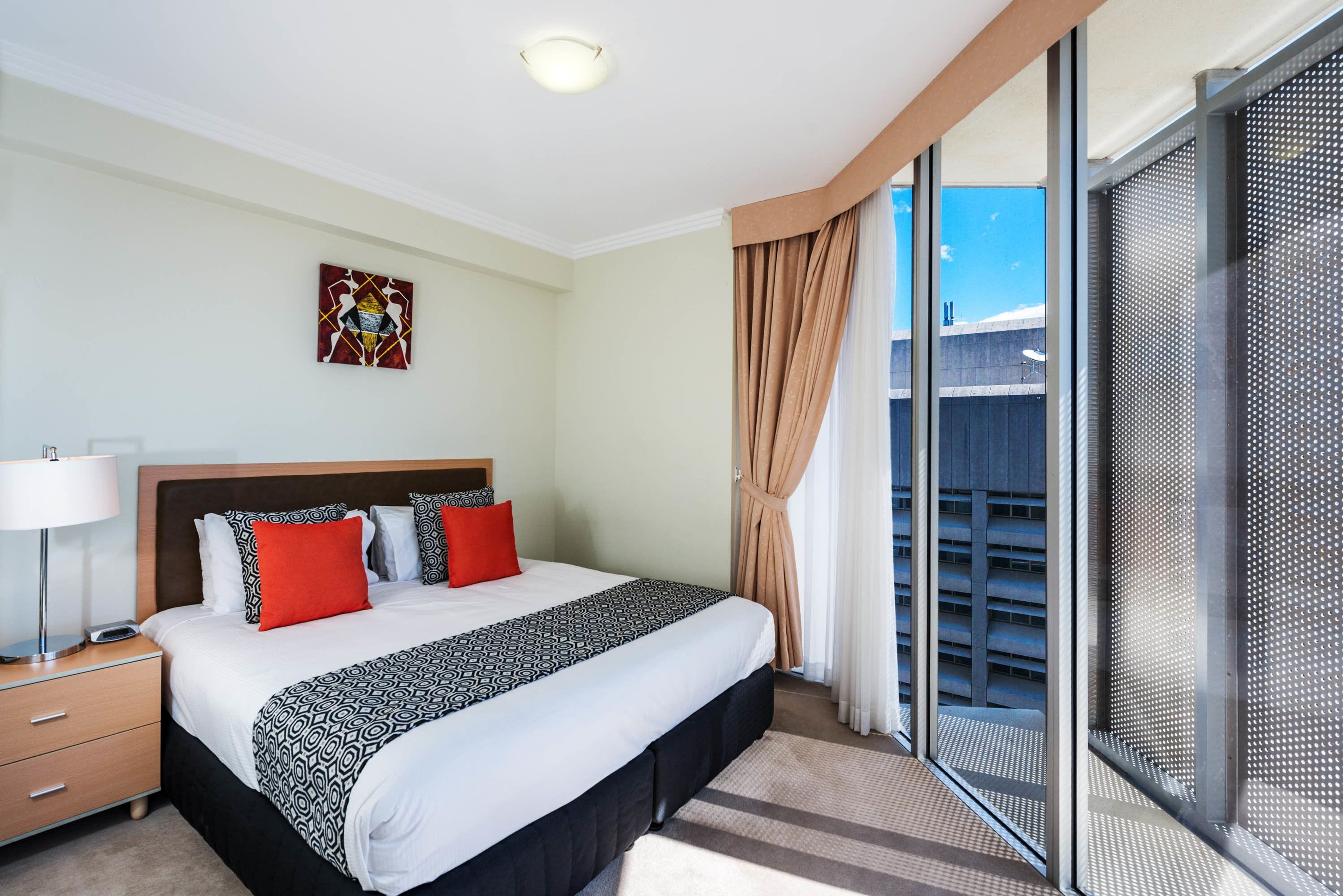 A hotel room with a large bed, a nightstand, a window with a view of the outside, and a ceiling light.