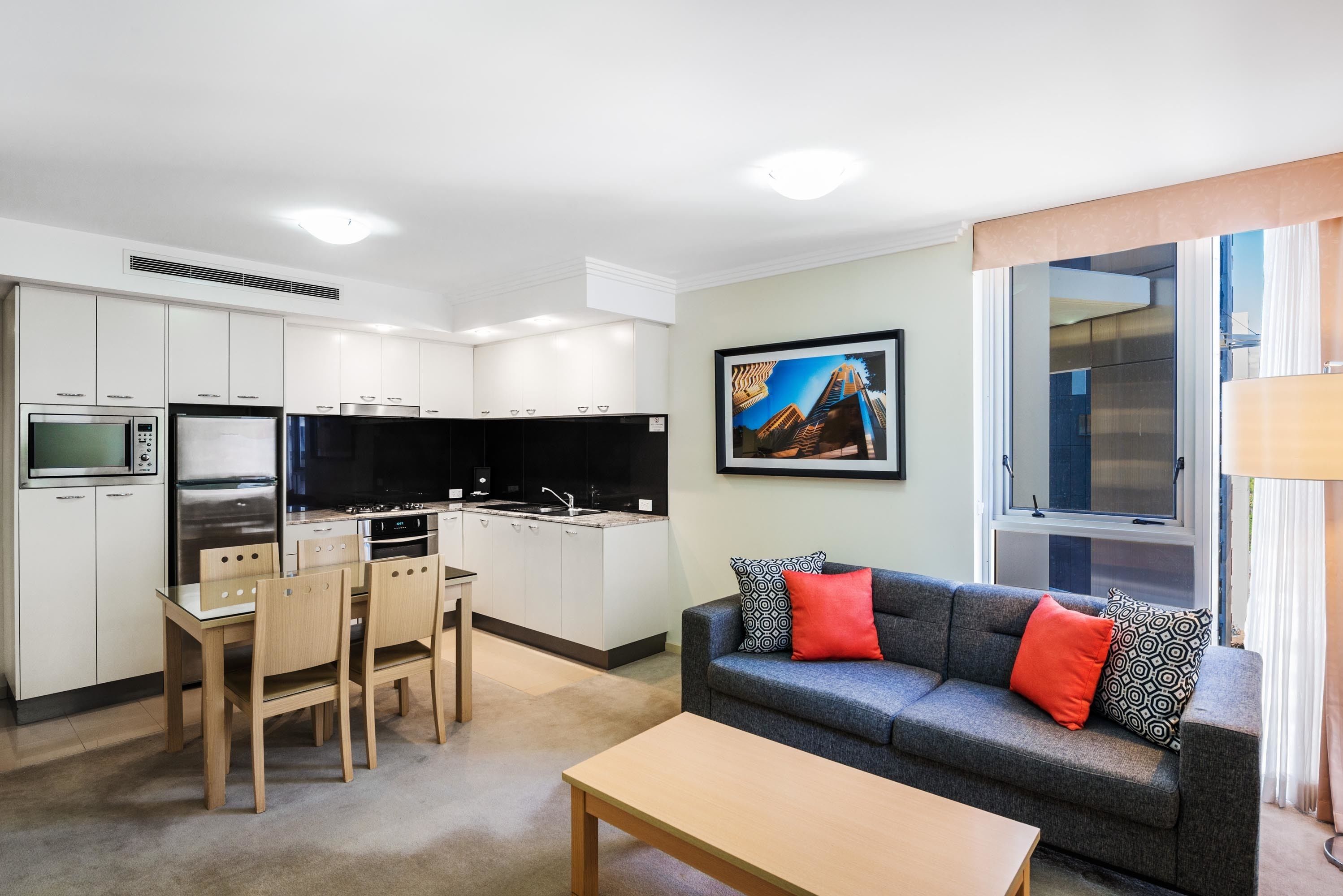 A compact living space with a kitchenette, a dining area, a sofa with patterned cushions, and a painting on the wall.