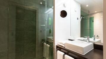 Uma casa de banho moderna com cabine de duche em vidro, lavatório branco e espelho grande.