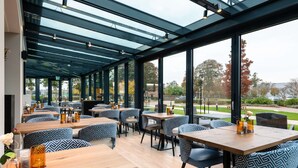 Un espace de restauration intérieur avec des tables et des chaises, de grandes fenêtres et un plafond en verre.
