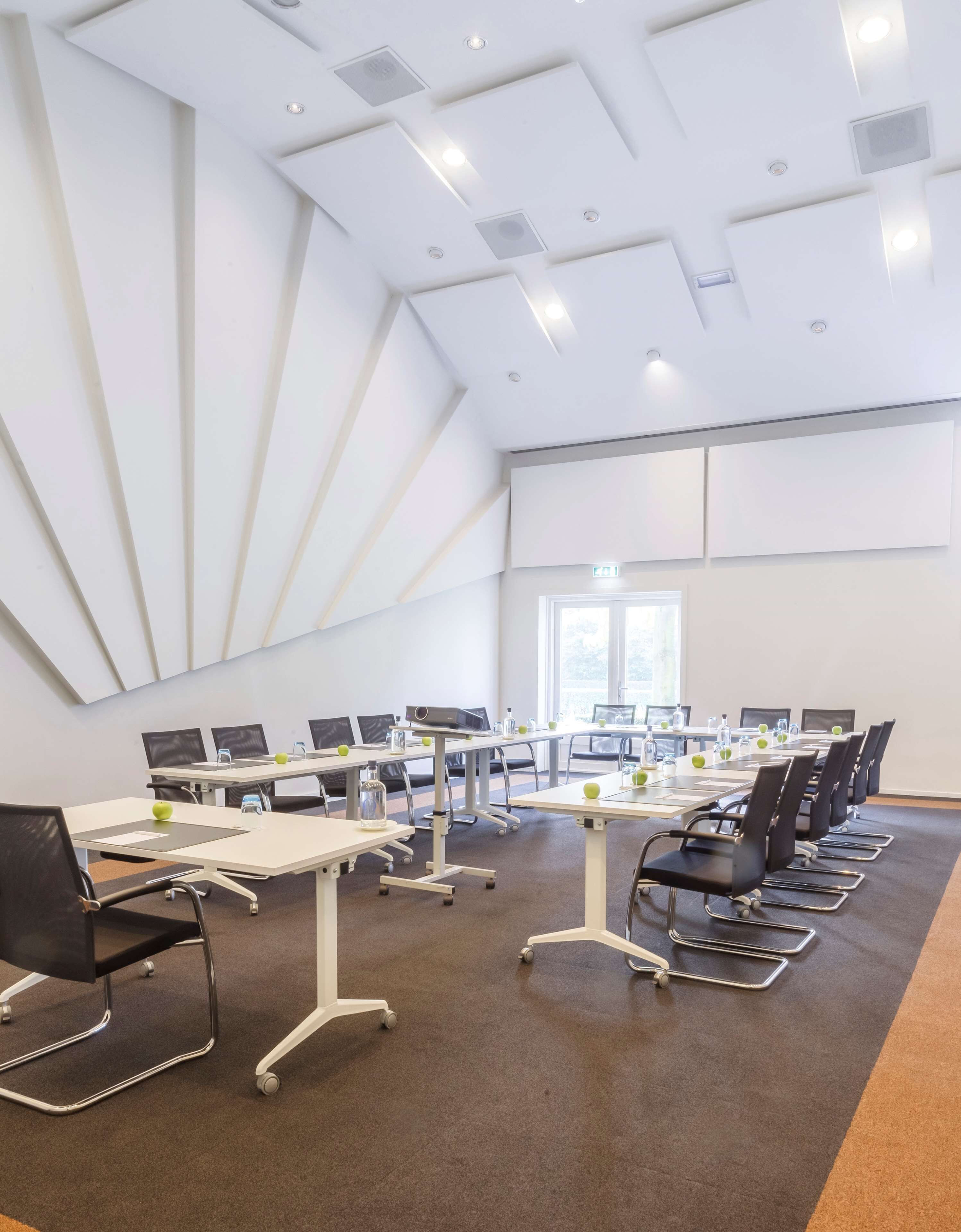 Une salle de conférence avec des tables et des chaises blanches, équipée d’ordinateurs portables, de bouteilles d’eau et de tranches de pommes.