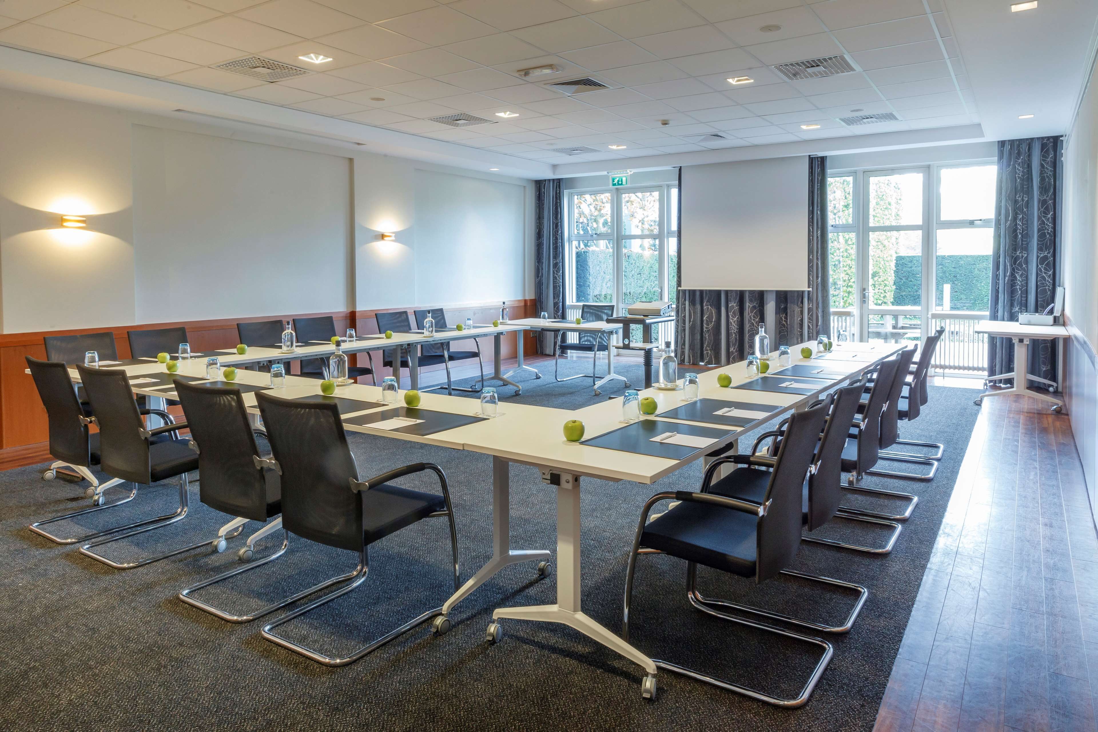 A conference room with a long table, chairs, and a projector screen.