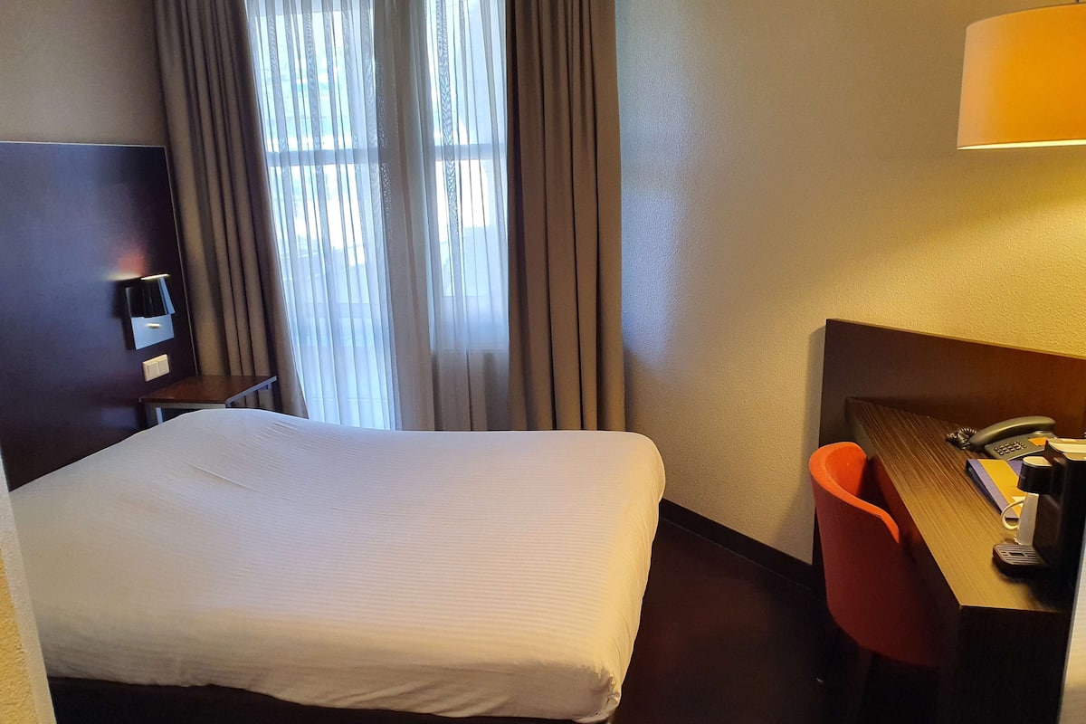 Een hotelkamer met een bed, een bureau met telefoon en een lamp.