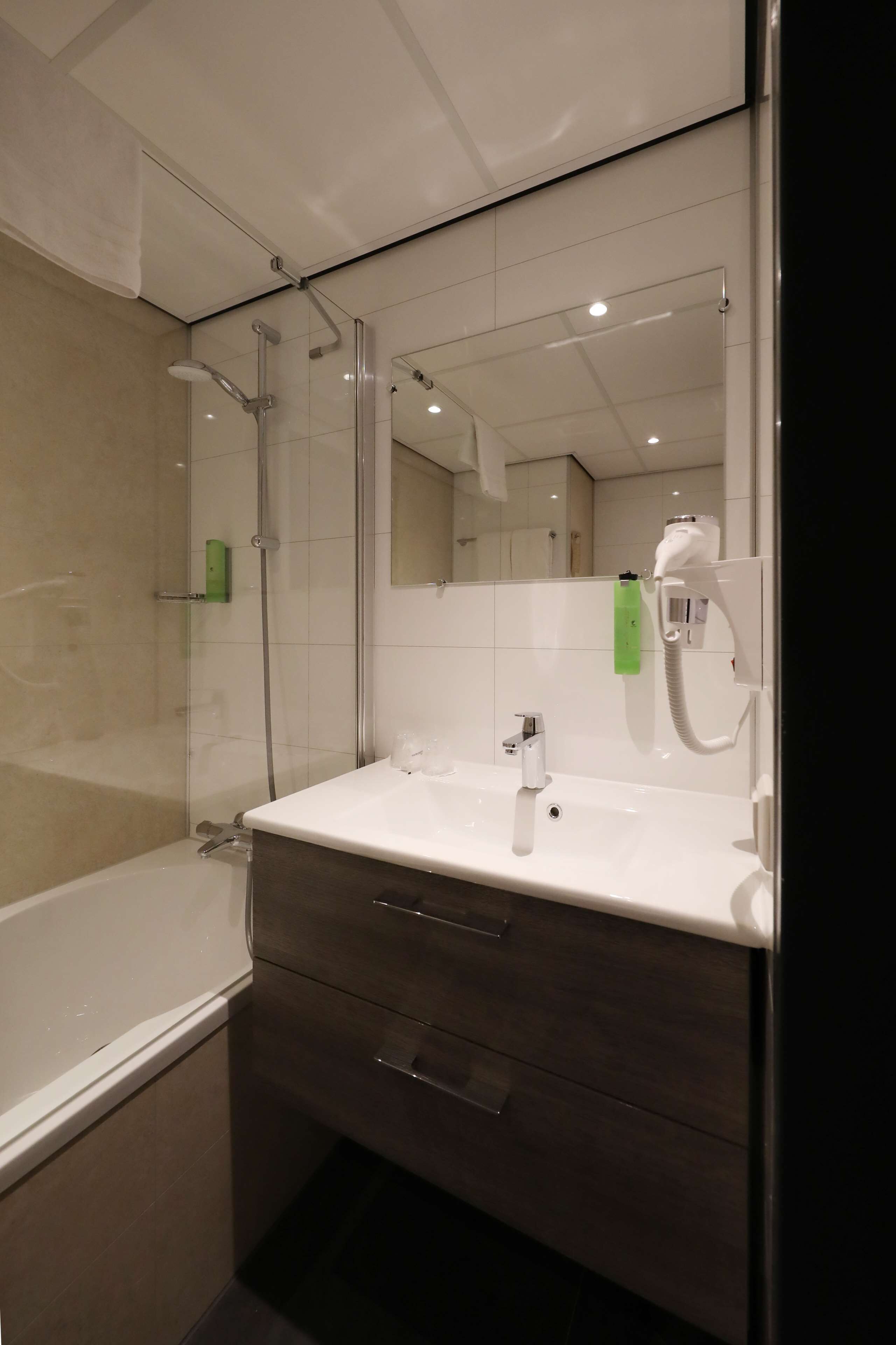 A modern bathroom with a glass shower enclosure, a white sink, a mirror, and a hairdryer.