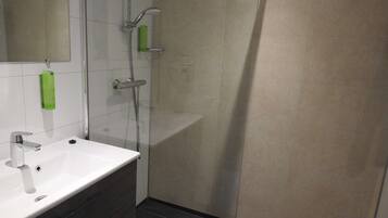 A modern bathroom with a white sink, a mirror, a glass shower enclosure, and a green soap dispenser.