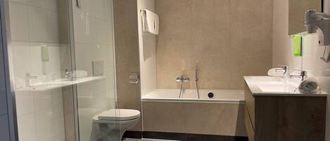Un baño moderno con ducha de vidrio, inodoro, bañera y tocador con espejo.