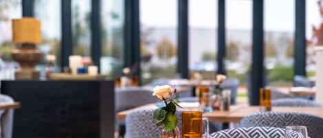 A restaurant with a table set for two, featuring a vase with a single flower, a candle, and a glass of water.
