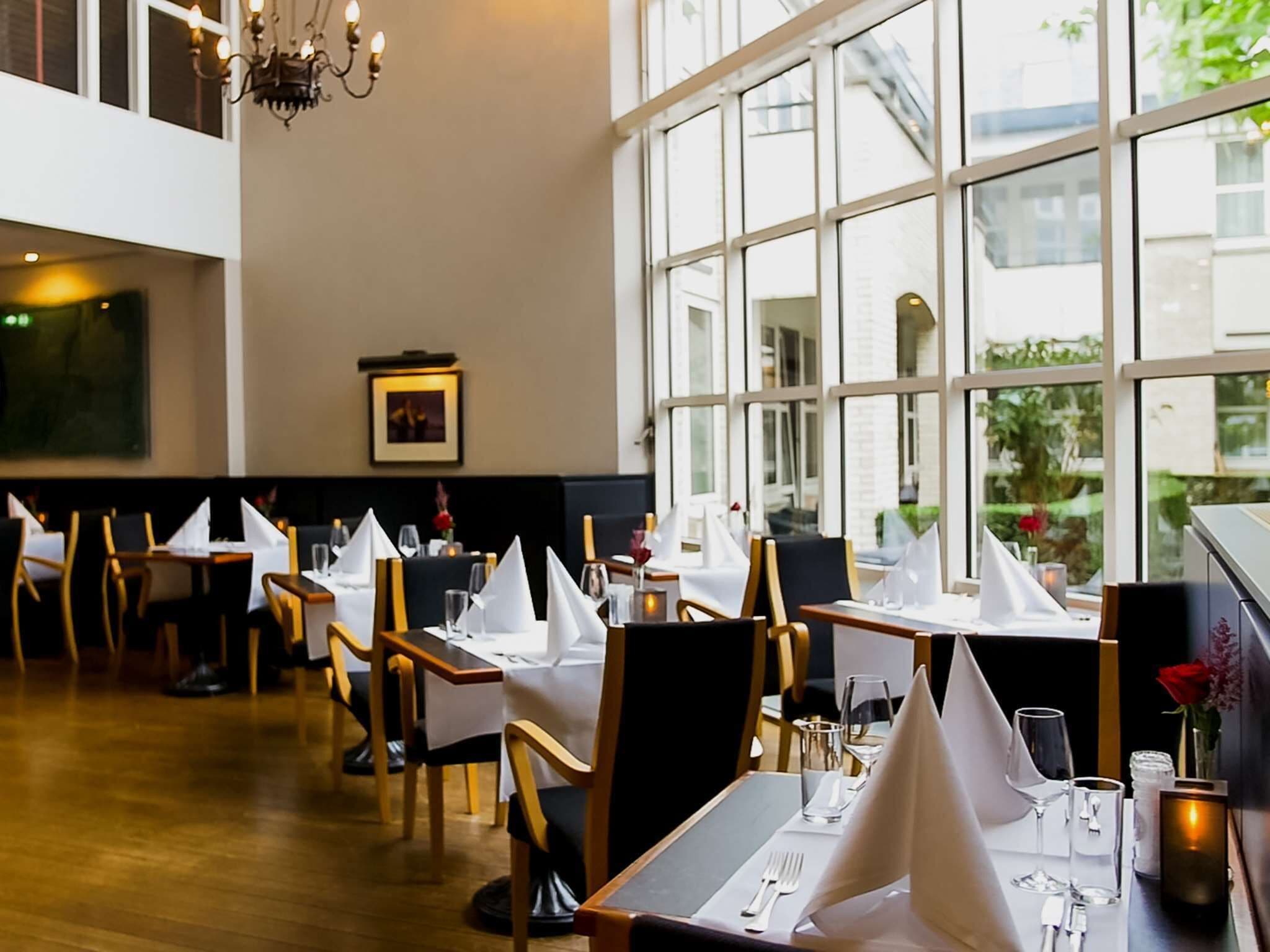 A restaurant with tables set for dining, large windows, and a chandelier.