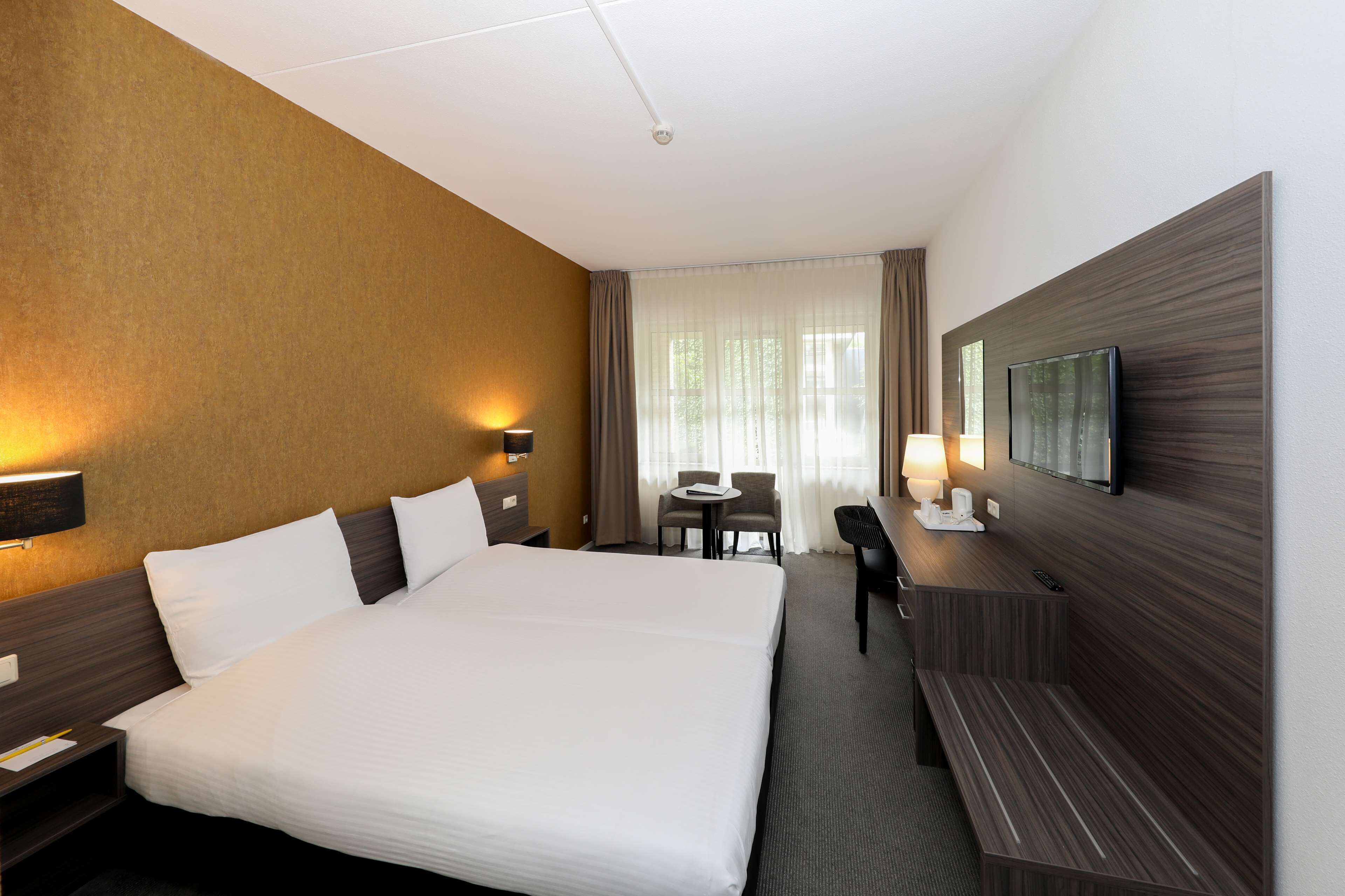 A hotel room with a large bed, a desk, a chair, and a television on the wall.