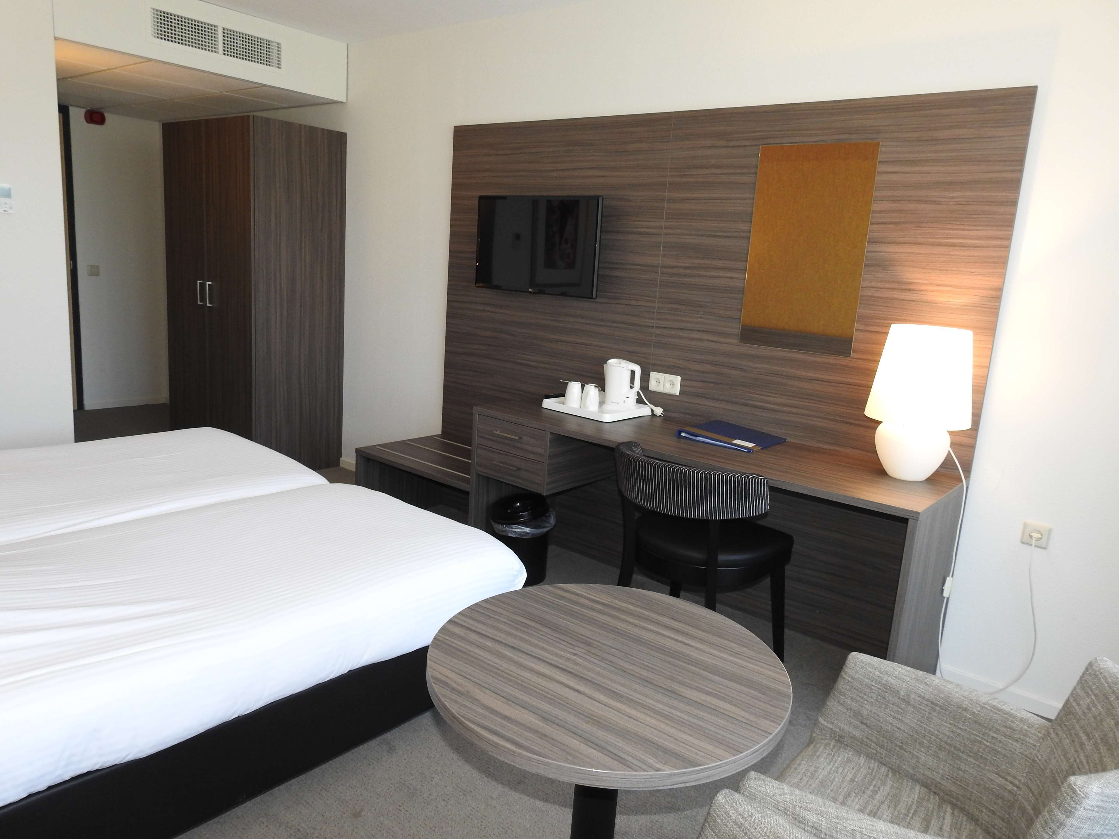 Una habitación de hotel con una cama, un escritorio con lámpara, un televisor y una mesita redonda.