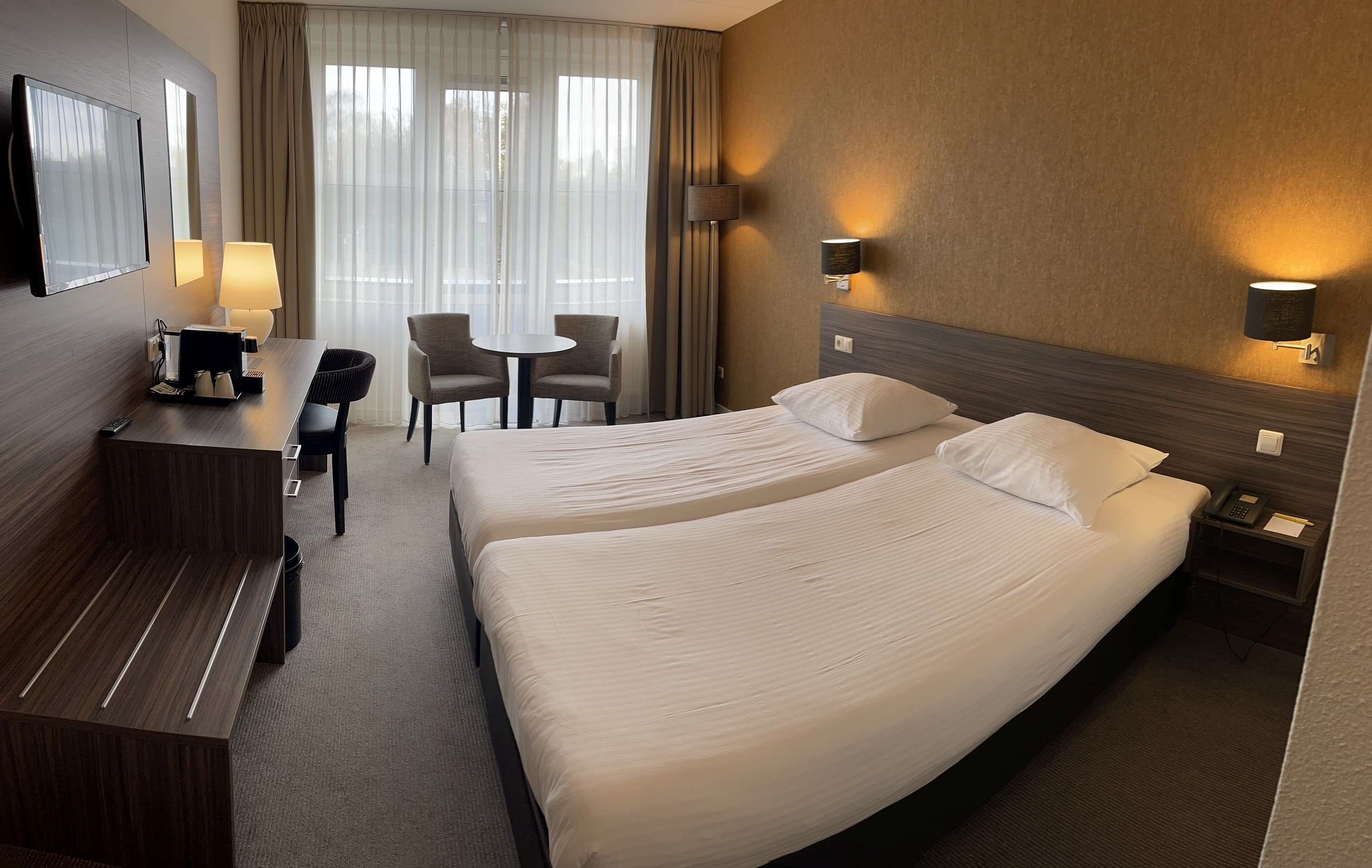 Ein Hotelzimmer mit zwei Betten, einem Schreibtisch mit Stuhl, einem kleinen Tisch und einem Fernseher.