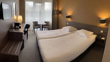 Ein Hotelzimmer mit zwei Betten, einem Schreibtisch mit Stuhl, einem kleinen Tisch und einem Fernseher.