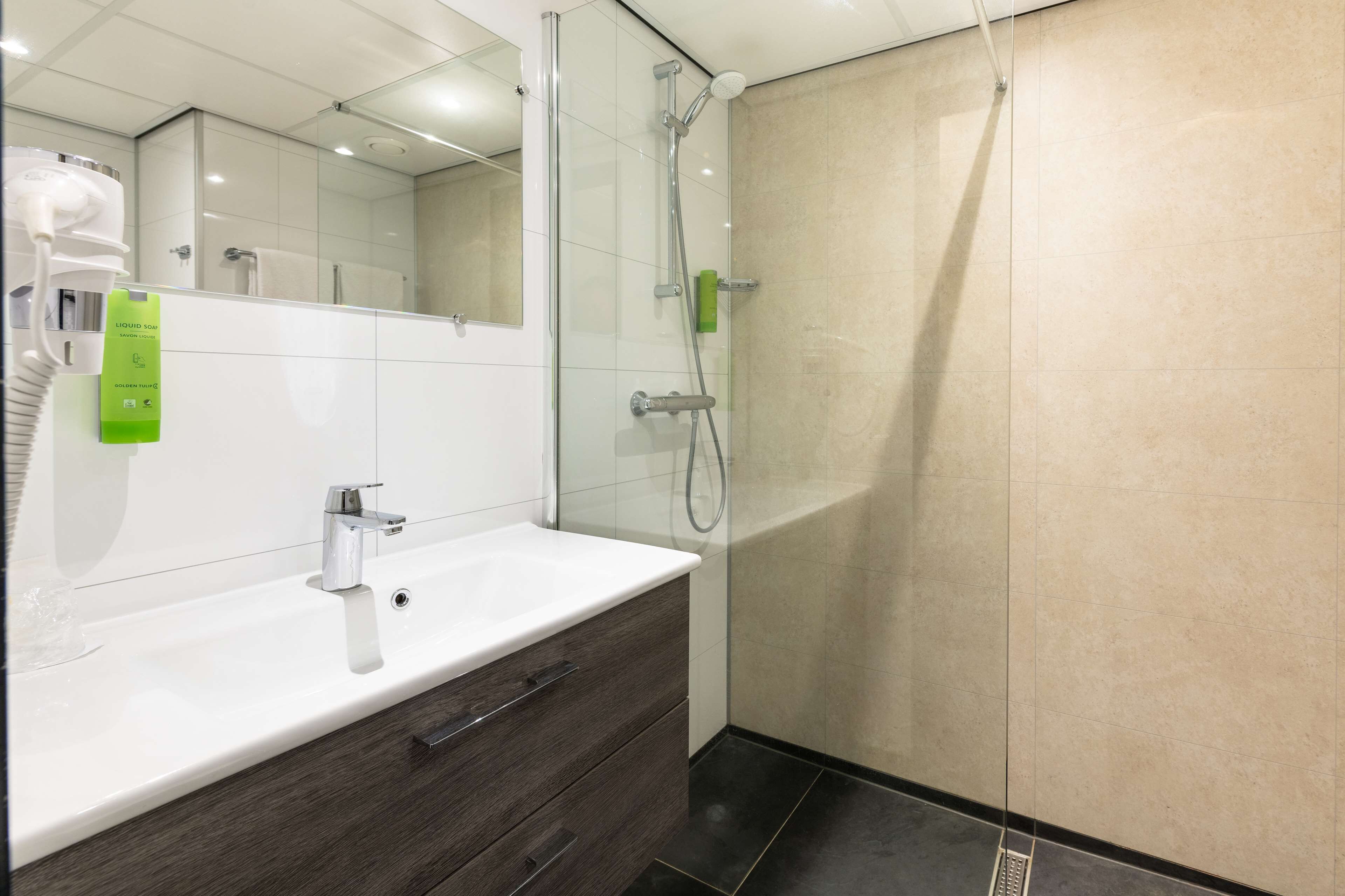 A modern bathroom with a white sink, dark wood vanity, a glass shower enclosure, and a mirror above the sink.