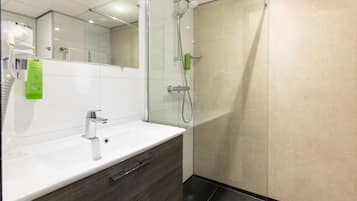 A modern bathroom with a white sink, dark wood vanity, a glass shower enclosure, and a mirror above the sink.