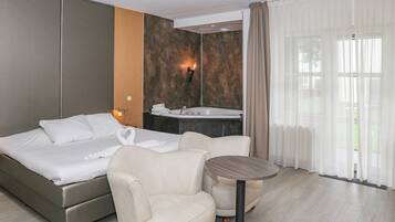 A hotel room with a bed, a seating area, a small table, a bathroom with a sink, and a large window with curtains.