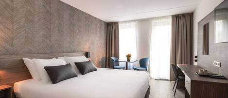 A modern hotel room with a large bed, a desk, and a chair.