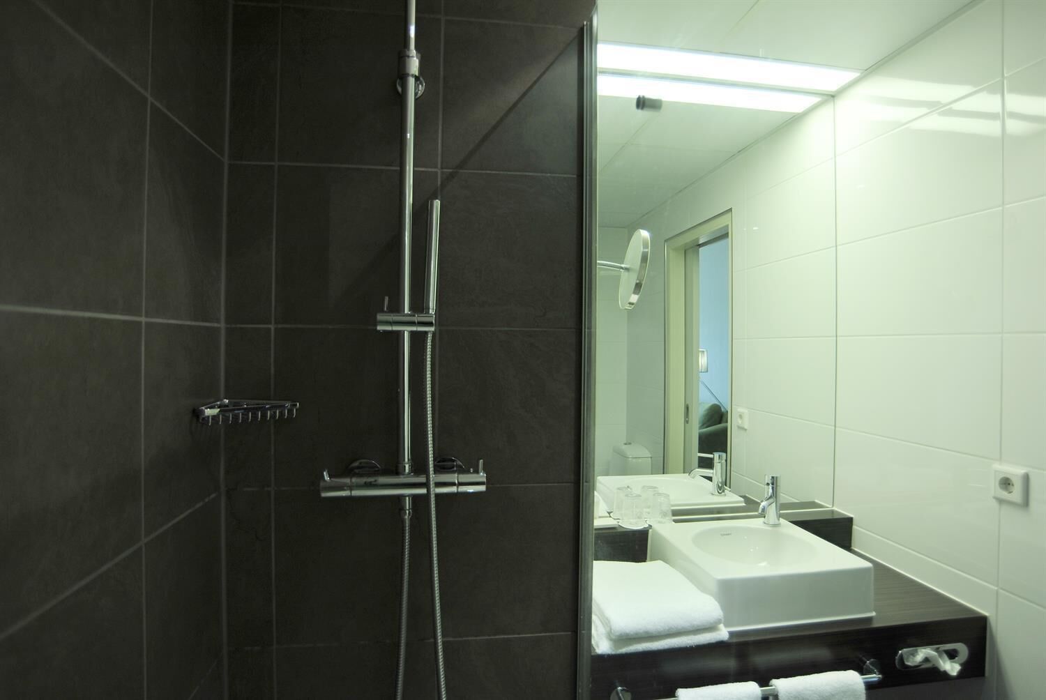 A modern bathroom with a dark tiled shower area, a glass-enclosed mirror, and a white sink with a countertop.