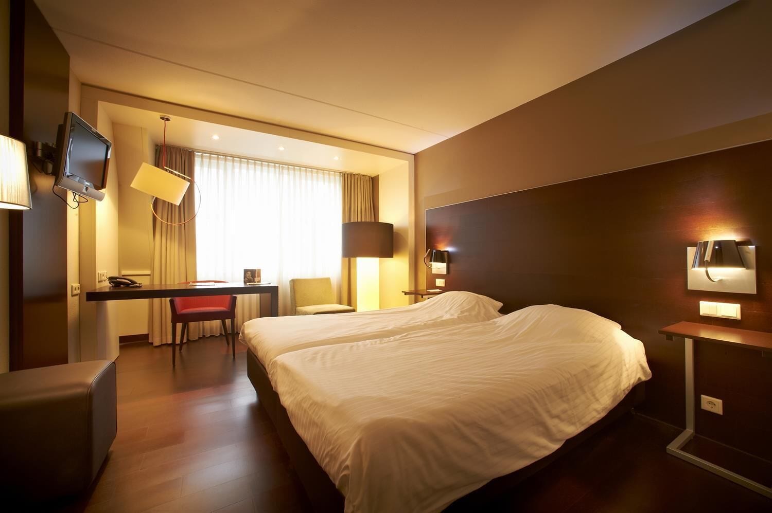 Une chambre d’hôtel avec deux lits, un bureau, une chaise, une télévision et une lampe.