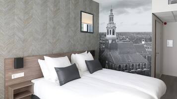 Ein modernes Hotelzimmer mit einem großen Bett, einem Nachttisch, einer Wandleuchte und einem Stadtbild-Wandgemälde.