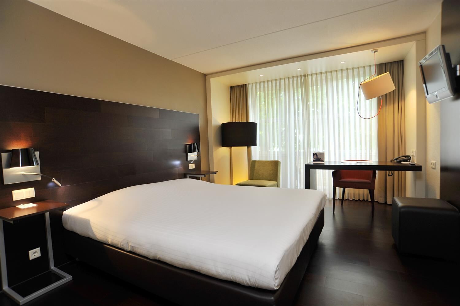 Une chambre d’hôtel avec un grand lit, un bureau avec une chaise, une télévision et une lampe.