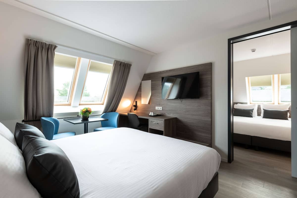 Een moderne hotelkamer met een groot bed, een bureau met stoel, een flatscreen televisie aan de muur en uitzicht op het groen.