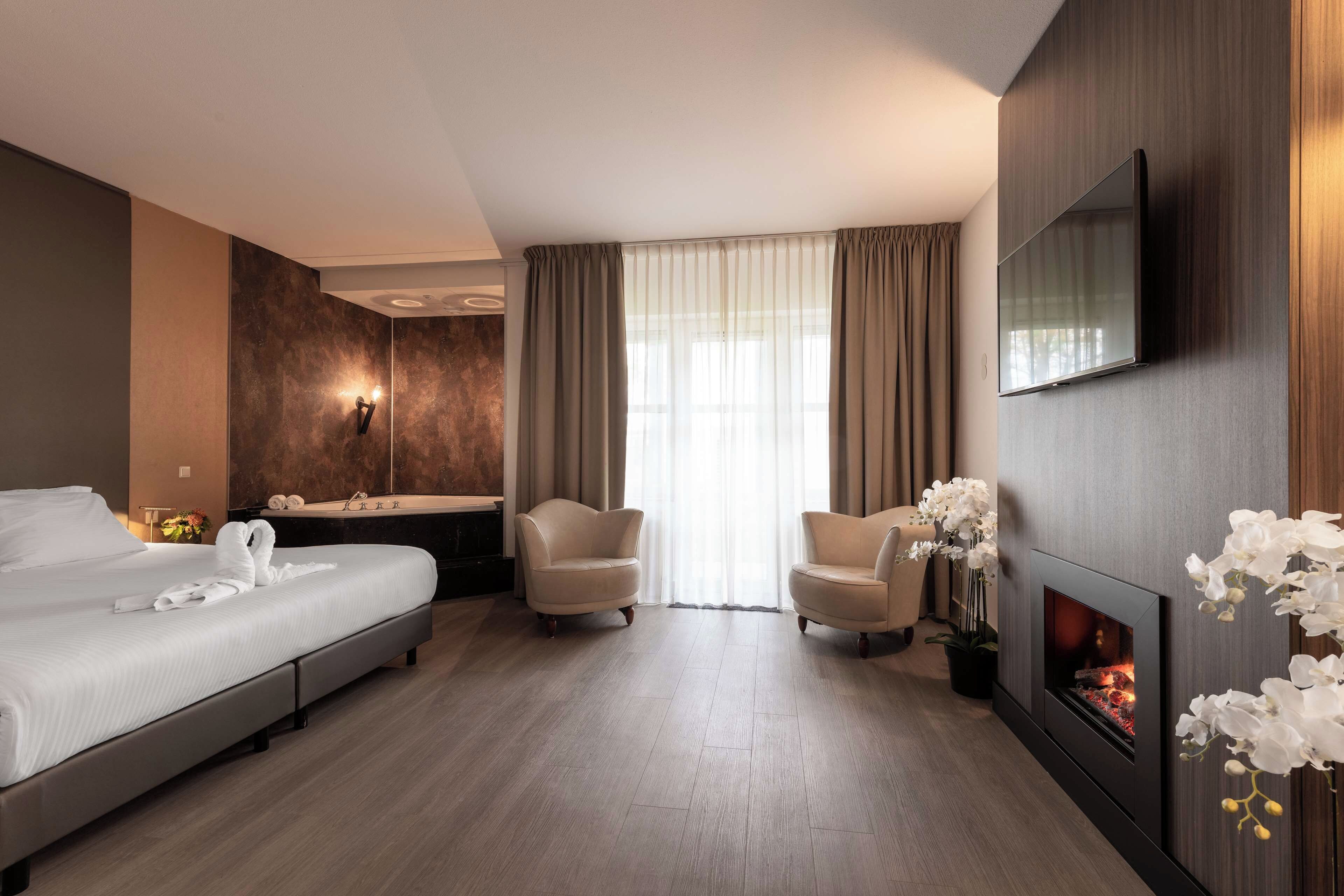 Una habitación de hotel con cama, sofá, sillón, chimenea y televisión.