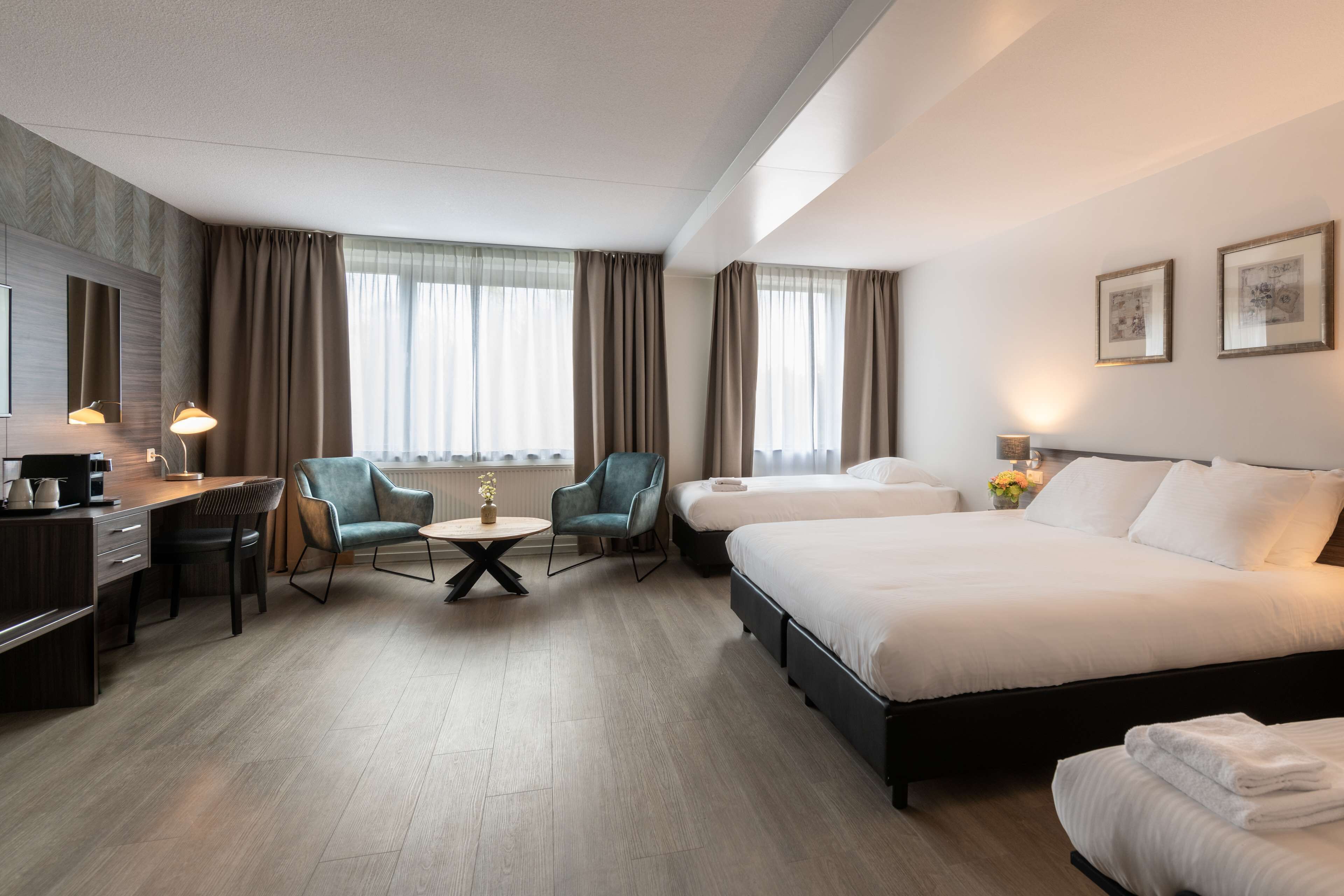 A hotel room with a bed, a desk, two chairs, a small table, and a window with curtains.
