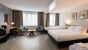 A hotel room with a bed, a desk, two chairs, a small table, and a window with curtains.