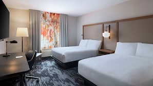 Een hotelkamer met twee bedden, een bureau, een stoel, een televisie en een raam met gordijnen.