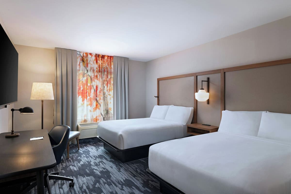 Een hotelkamer met twee bedden, een bureau, een stoel, een televisie en een raam met gordijnen.