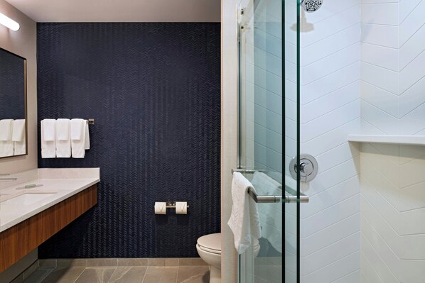 A modern bathroom with a dark patterned wall, a glass shower enclosure, and a white tiled floor.