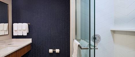 A modern bathroom with a dark patterned wall, a glass shower enclosure, and a white tiled floor.