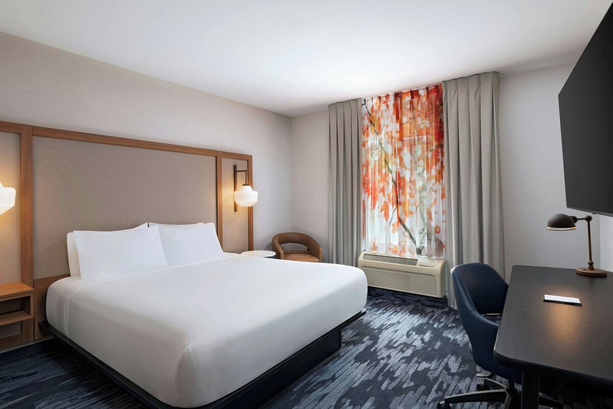 Hotelkamer met een groot bed, een bureau, een stoel, een televisie en een raam met gordijnen.