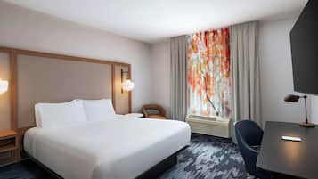 Une chambre d’hôtel avec un grand lit, un bureau, une chaise, une télévision et une fenêtre avec des rideaux.