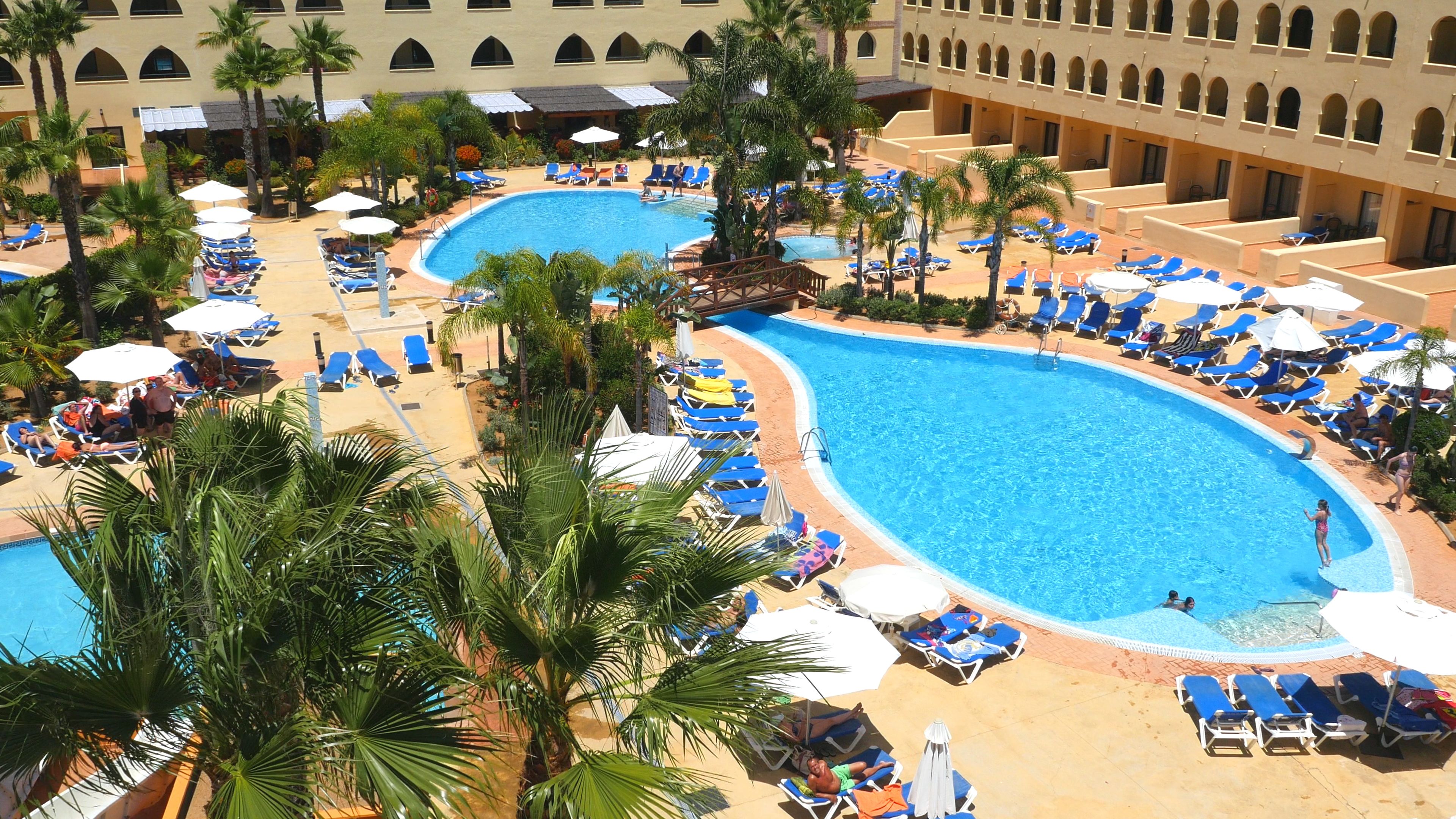 A resort with multiple swimming pools, sun loungers, and palm trees.