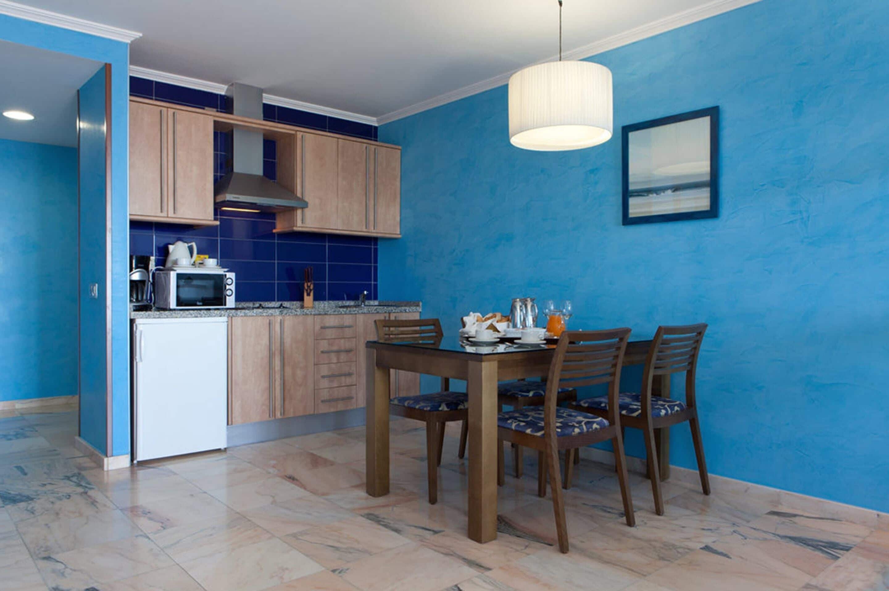 Eine Küche mit blauen Wänden, Holzschränken, einem weißen Kühlschrank und einem Esstisch mit Stühlen.
